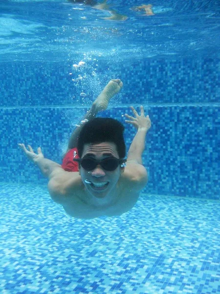 Tiro vertical de uma pessoa vestindo maiô vermelho e óculos nadando debaixo d 'água — Fotografia de Stock
