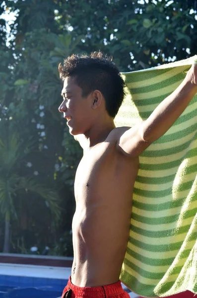 Tiro vertical de un macho sosteniendo su toalla cerca de la piscina con un fondo borroso — Foto de Stock
