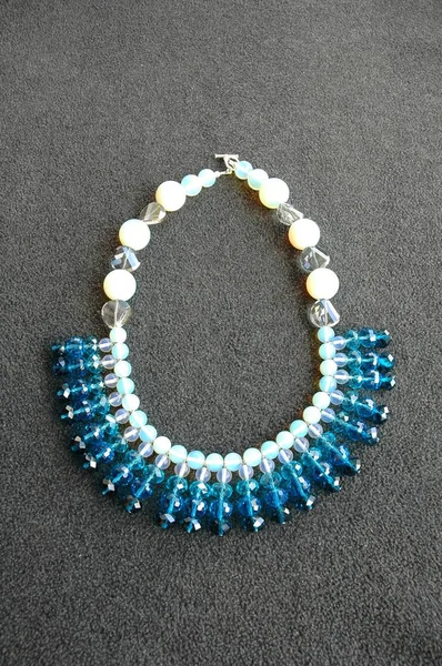 Tiro vertical de un collar de perlas blancas y azules sobre una superficie gris —  Fotos de Stock