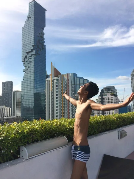 Άνδρας που φοράει μαγιό και στέκεται σε μπαλκόνι με θέα σε κτίρια και αφηρημένους ουρανοξύστες — Φωτογραφία Αρχείου