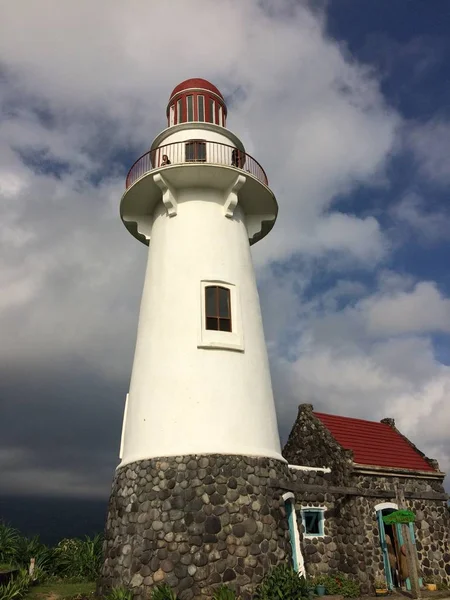 Vertical shot of a white and red lighthouse near a stone cabin under a cloudy sky — Stock Photo, Image