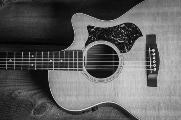 Belo tiro em tons de cinza de uma guitarra acústica apoiada em uma porta de madeira em uma superfície de madeira — Fotografia de Stock
