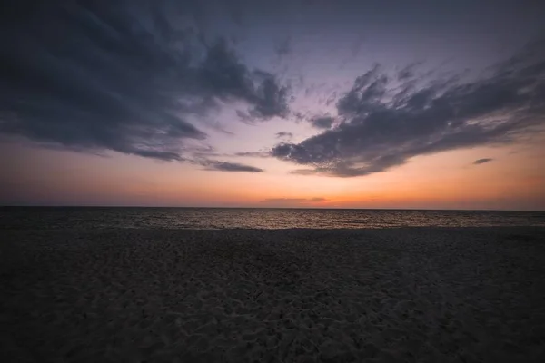 Beautiful shot of a sandy surface near the sea under an orange and blue sky at sunset — Stock Photo, Image