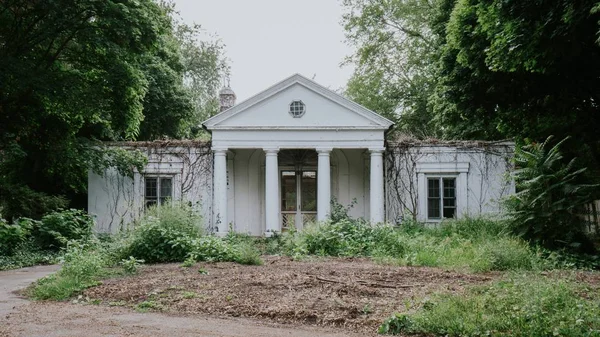 Verlaten wit huis omgeven door bomen en groen gras — Stockfoto