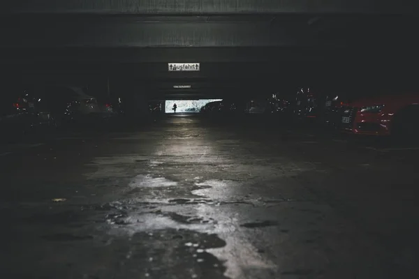 Low angle shot of an underground parking lot with a lot of cars and an exit sign — 스톡 사진