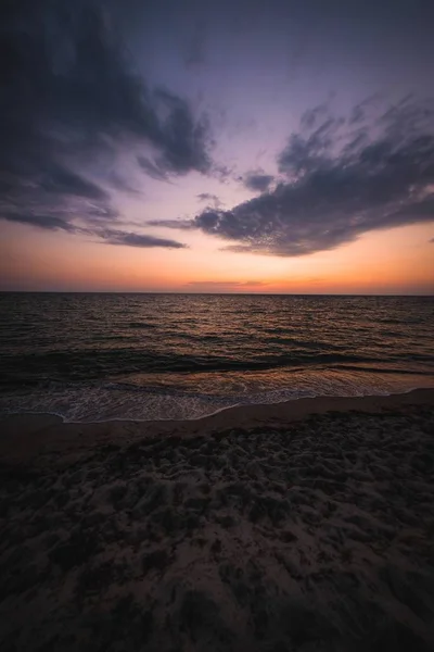 Вертикальний знімок пляжного берега під помаранчевим і блакитним небом на заході сонця — стокове фото