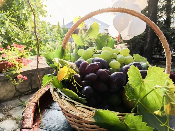 Zdjęcia z bliska ze słomkowym koszem pełnym białych winogron i śliwek z białymi balonami z tyłu — Zdjęcie stockowe