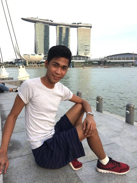 Foto vertical de una persona sentada junto al agua cerca de los hoteles Marin Bay Sands en Singapur. —  Fotos de Stock