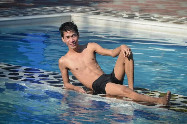 Masculino usando maiô preto deitado em um lado da piscina posando para a câmera — Fotografia de Stock