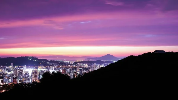 Silhuett av en kulle nära stadshus under en ljusrosa himmel vid midnatt — Stockfoto