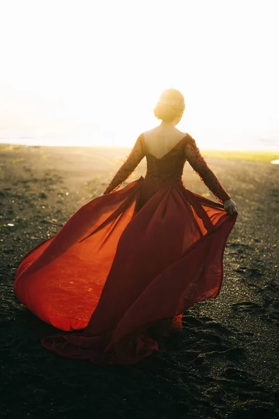 Junge Frau mit einem schönen roten langärmeligen Kleid am Strand während des Sonnenuntergangs — Stockfoto