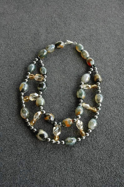 Tiro vertical de un collar de perlas marrones y grises sobre una superficie gris — Foto de Stock
