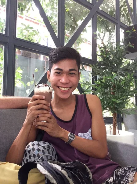 Tiro vertical de um macho sorrindo e segurando seu smoothie chocolate sentado em um café — Fotografia de Stock