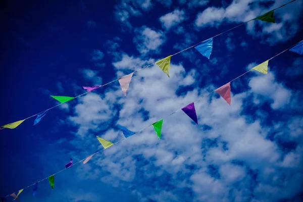 Plan à angle bas de drapeaux de différentes couleurs sur une corde avec un ciel nuageux bleu en arrière-plan — Photo
