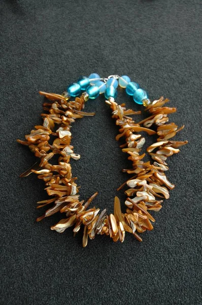Tiro vertical de um colar feito de conchas de puka marrons e contas azuis em uma superfície cinza — Fotografia de Stock