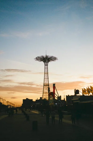 Gün batımında parkta yürüyen insanlarla birlikte metalik bir kulenin dikey görüntüsü. — Stok fotoğraf