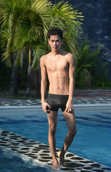 Prise de vue d'un homme portant un maillot de bain noir debout sur le bord d'une piscine sur le fond de plantes tropicales — Photo