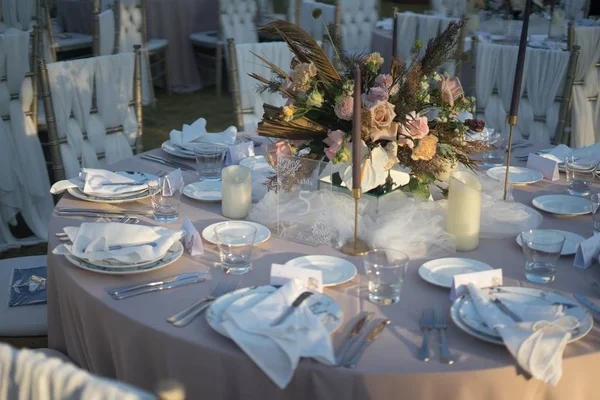 결혼식 피로연을 위해 흰 접시, 양초, 꽃으로 식탁을 준비하는 장면을 클로즈업으로 찍은 사진 — 스톡 사진