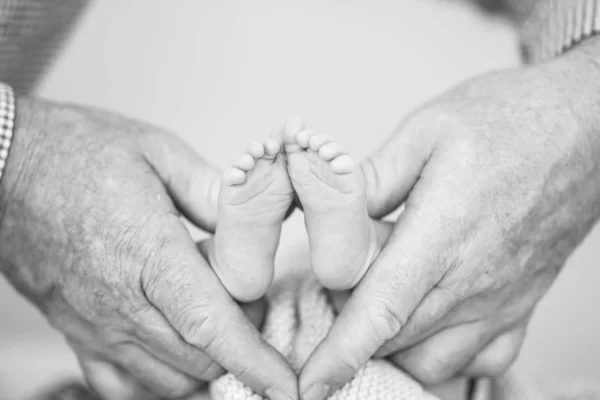 Closeup greyscale shot of human hands holding a newborn's feet — Stock Photo, Image