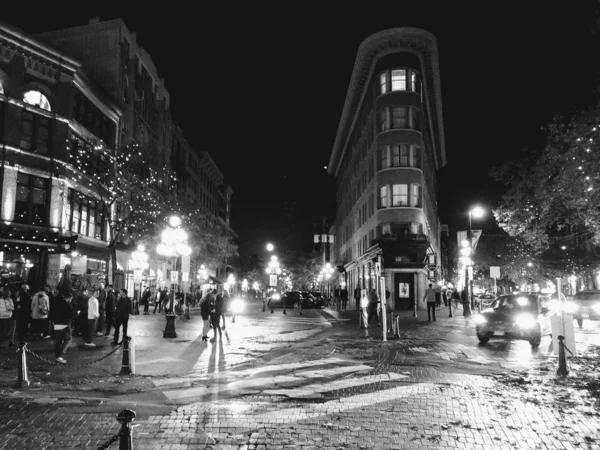 Greyscale horizontal shot of a city center during the night with cars and people passing by — Stock Photo, Image