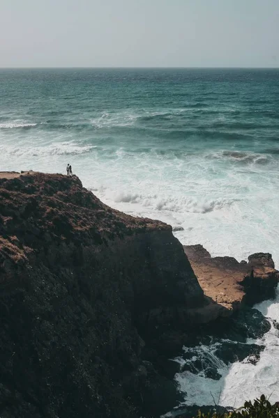 Vertikalt skott av människor som står på klippan nära havet under dagtid — Stockfoto