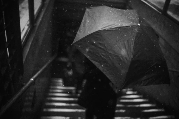 Closeup high angle grayscale shot of a person holding a large umbrella on the stairway during Winter — Stock Photo, Image