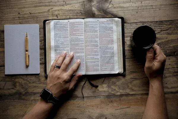 Kopfschuss eines Mannes, der seinen Kaffeebecher in der Hand hält und ein Buch auf einer Holzoberfläche liest — Stockfoto