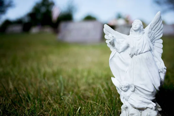 Plan rapproché d'une statue d'ange sur un terrain herbeux avec un fond flou — Photo