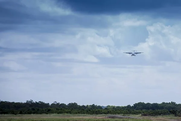 Beautiful shot of an airplane above the grassy field and trees with a cloudy sky in the background — Stock Photo, Image