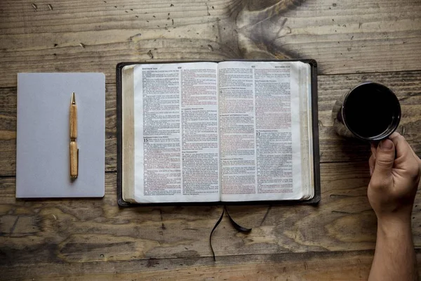 Boven foto van een man met zijn koffiemok in de buurt van een open boek op een houten oppervlak — Stockfoto