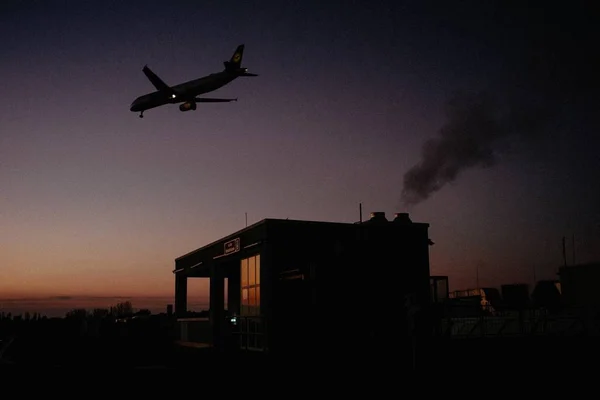 ドイツの日没時に小さな建物の上を飛行する飛行機の暗いショット — ストック写真