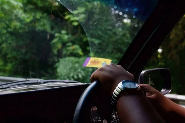 Tiro de perto das mãos segurando o volante com árvores visíveis através do pára-brisas — Fotografia de Stock