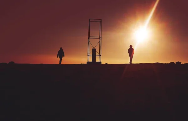 Silhouette von zwei Personen in der Nähe des grauen Metallrahmens bei Sonnenuntergang — Stockfoto