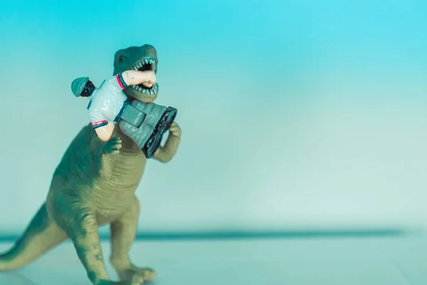 Closeup shot of a miniature toy dinosaur eating a toy human figurine on a light blue background — Stock Photo, Image