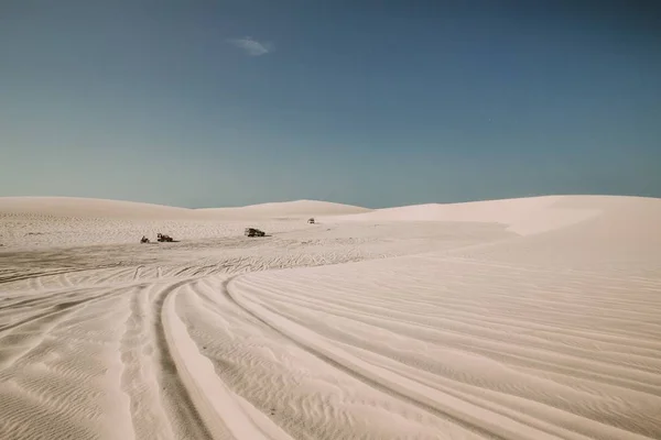 Paisaje plano de un desierto con marcas de neumáticos en la arena y vehículos de motor en la distancia — Foto de Stock