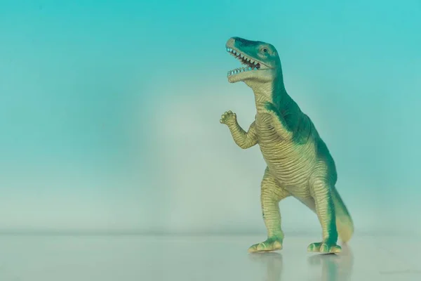 Close-up tiro de um dinossauro brinquedo miniatura rugindo em um azul claro — Fotografia de Stock