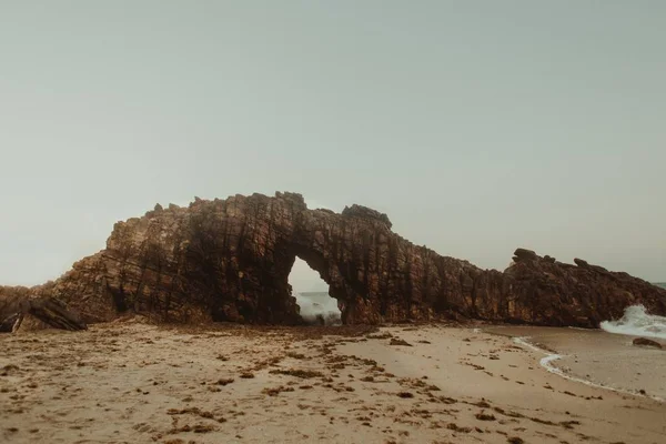 Paesaggio di una scogliera con un arco su una spiaggia di sabbia — Foto Stock