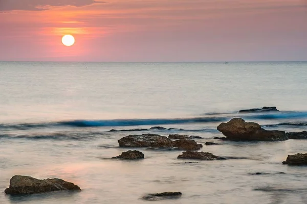 Horizontal shot of a body of water with rocks near the shore during sunset — Stock Photo, Image