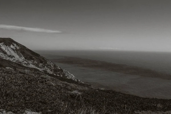 Grayscale tiro de colinas cobertas de grama pelo mar — Fotografia de Stock