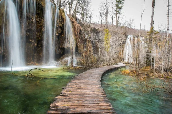 Horizontal shot of a wooden pathway on a body of water with waterfalls flowing from the cliffs — Stock Photo, Image