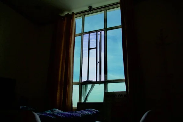 Ciemne ujęcie wnętrza pokoju z łóżkiem i niebem widocznym przez duże okno — Zdjęcie stockowe