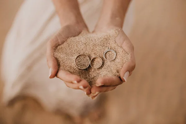 Gros plan de mains féminines tenant du sable avec trois anneaux sur le dessus — Photo