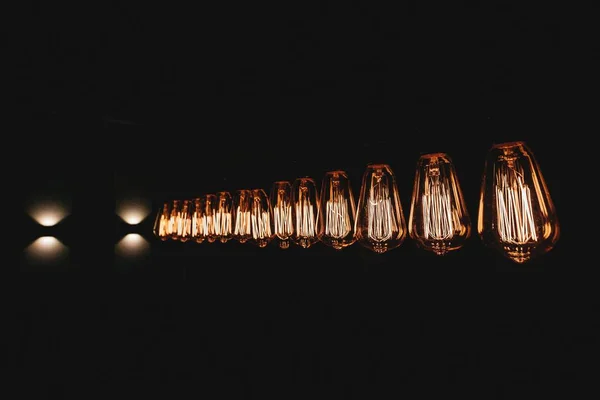 Tiro horizontal de lâmpadas velhas alinhadas lançando uma luz fraca no quarto escuro — Fotografia de Stock