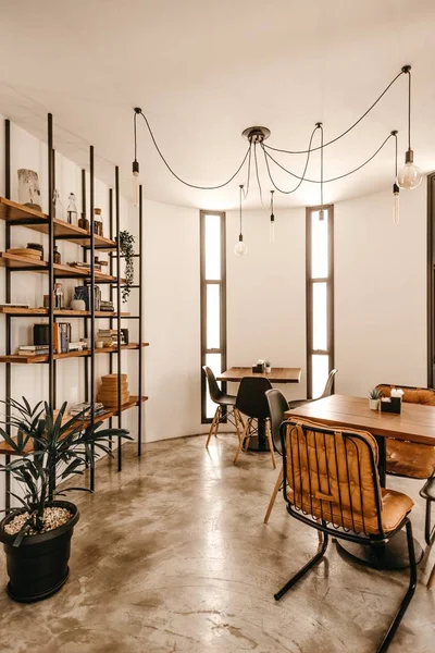 Vertical shot of a cafe interior with tables, chairs, and  a bookshelf near the wall — Stock Photo, Image