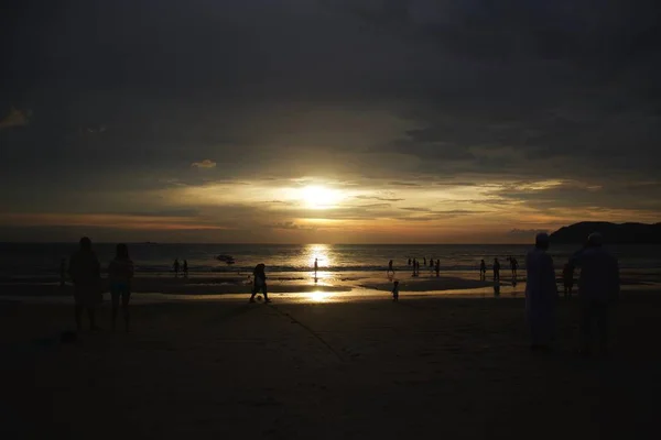 Foto horizontal de la playa y el mar al atardecer con gente caminando por la playa — Foto de Stock
