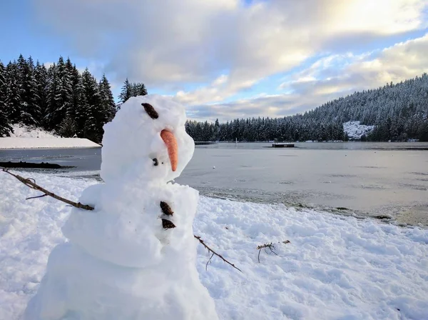 Closeup shot of a deformed snowman with a frozen lake in the background during winter — Stock Photo, Image