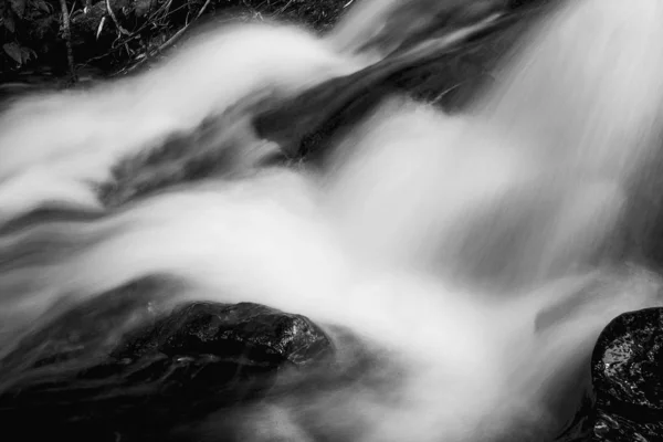 Closeup grayscale shot de uma cachoeira espumosa que flui através de rochas — Fotografia de Stock