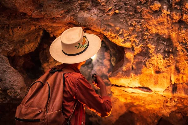 Horizontal shot of a female with a hat walking with a flashlight in the cave — Stock Photo, Image