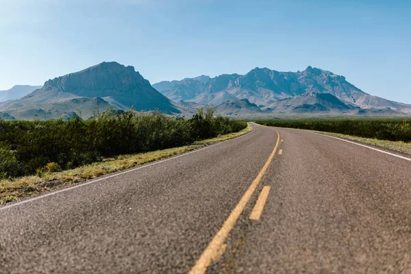 Schöne Aufnahme einer leeren Straße inmitten von Pflanzen und Bergen in der Ferne — Stockfoto