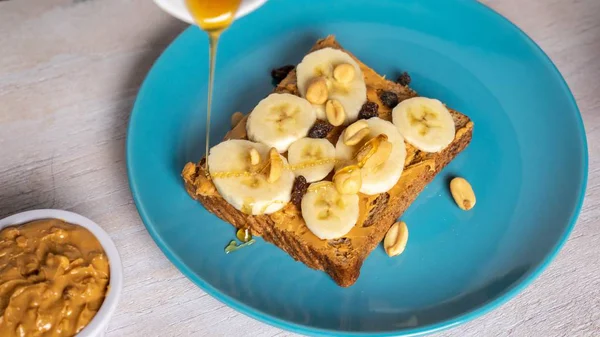Selektive Nahaufnahme eines Toastes mit Erdnussbutter, verschiedenen Samen, Honig und Bananen — Stockfoto